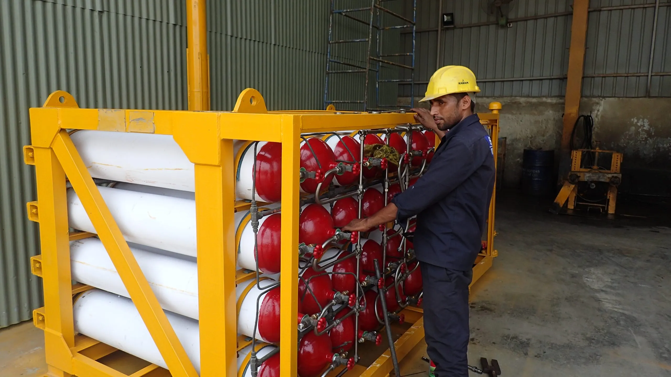 A technician inspecting a yellow-framed CNG cascade of red cylinders