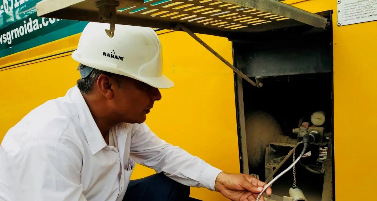 A PLS technician checking the CNG fittings on a yellow bus for leaks